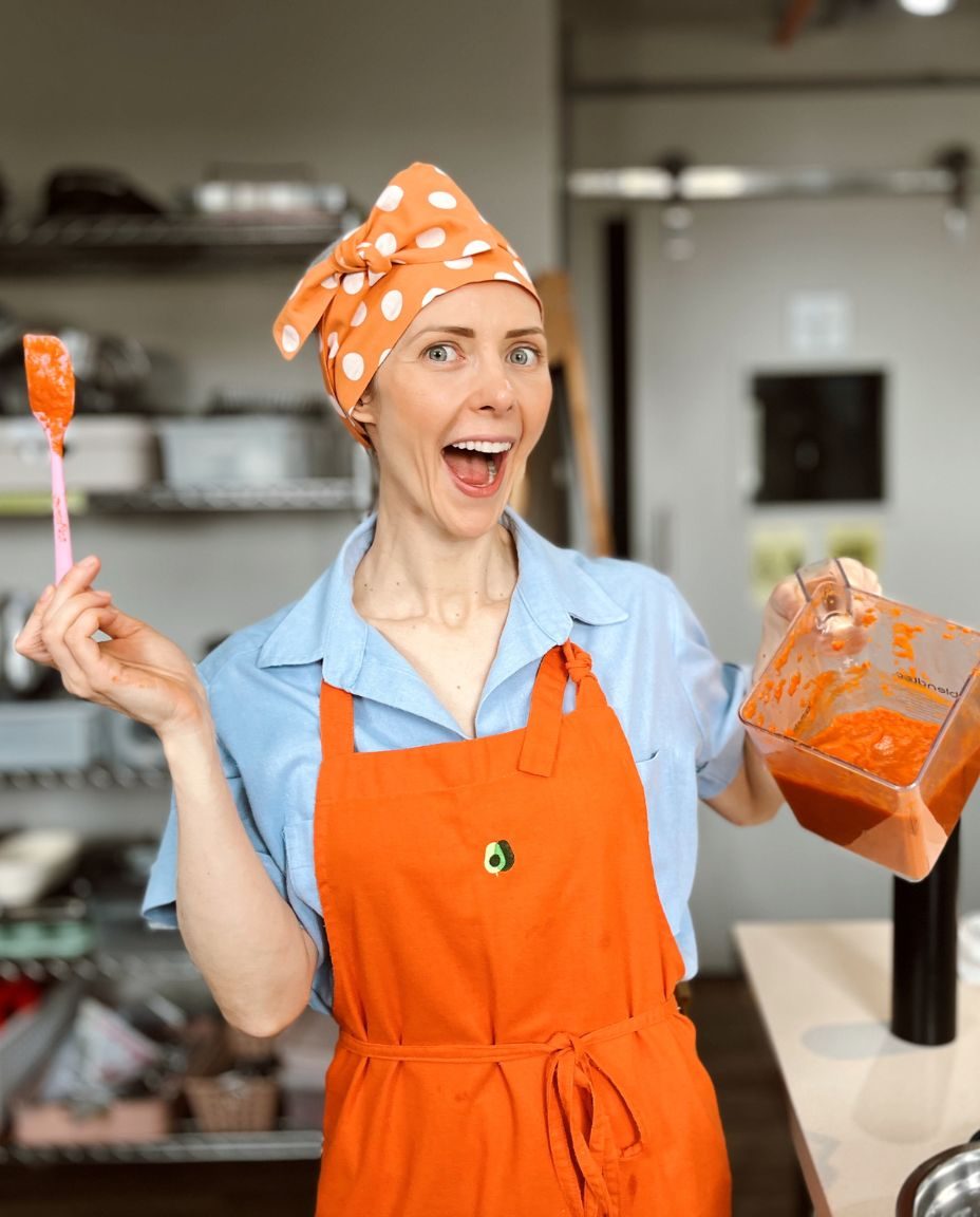 Fran Tonello sorrindo na cozinha, de avental, com o liquidificador na mão